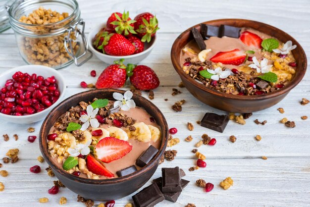 Chocolate smoothie bowl topped with oat granola banana strawberries pomegranate and spring flowers