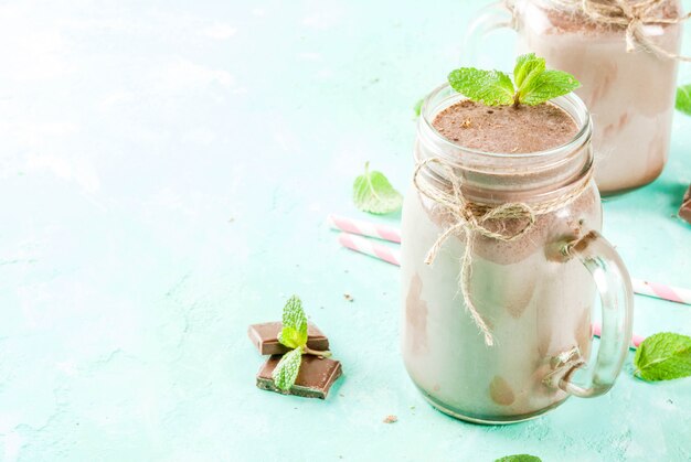 Chocolate smoothie or milkshake with mint and straw, in mason jar on light blue background,