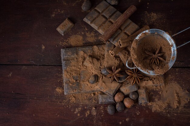 Chocolate, Spices, Spoon with Cocoa, Metal Strainer, Hazelnut on Dark Wooden surface. Copy space. Flat lay, top view