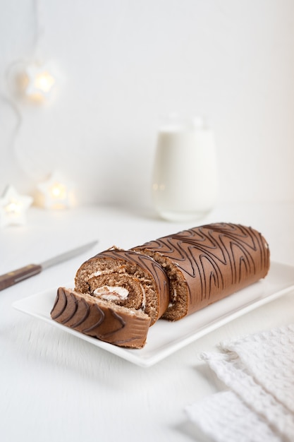 Chocolate sponge roll cake or roulade with cream sliced with knife, textile towel and glass of milk