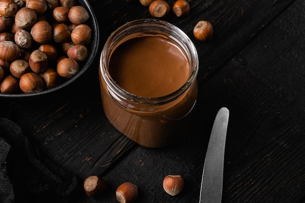 Chocolate spread or nougat cream with hazelnut set on black wooden table background