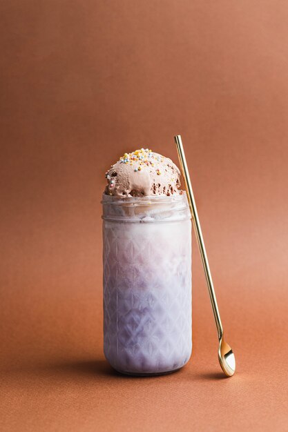 Chocolate, strawberry and blueberry ice cream in the glass with pastel colorful confetty topping with gold spoon on brown background. close up with copyspace. still life