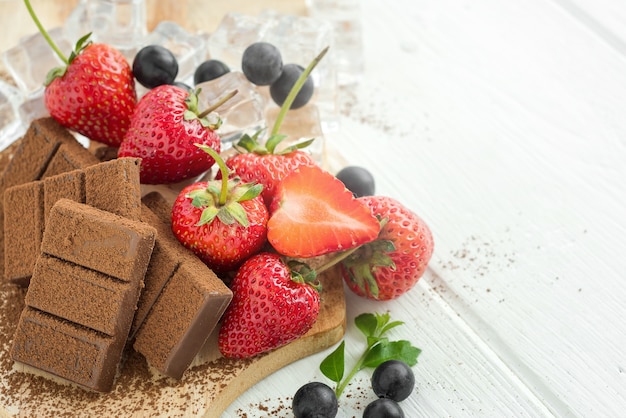 Chocolate, strawberry, blueberry and ice cubes on wooden plate