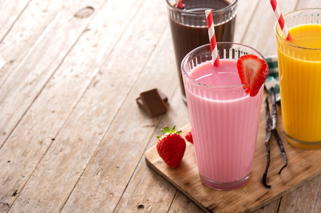 Chocolate, strawberry and vanilla milkshakes on rustic wooden table