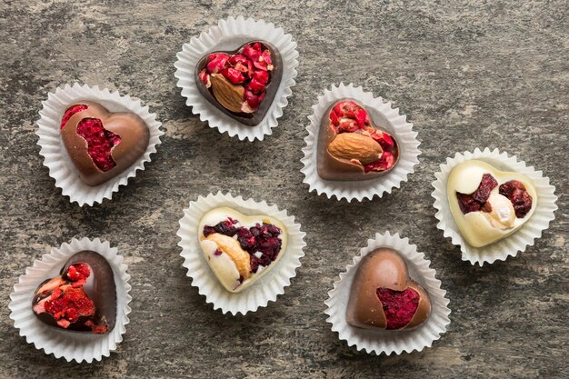 chocolate sweets in the form of a heart with fruits and nuts on a colored background top view with space for text holiday concept