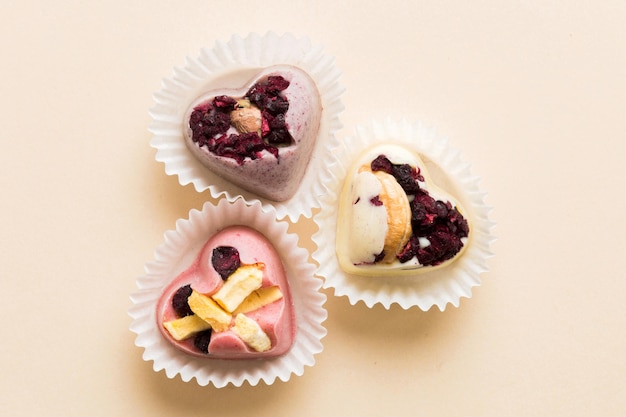 chocolate sweets in the form of a heart with fruits and nuts on a colored background top view with space for text holiday concept