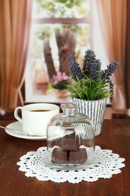 Chocolate sweets under glass cover and hot drink on bright background