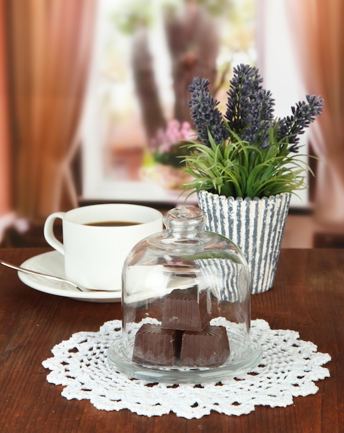 Chocolate sweets under glass cover and hot drink on bright background