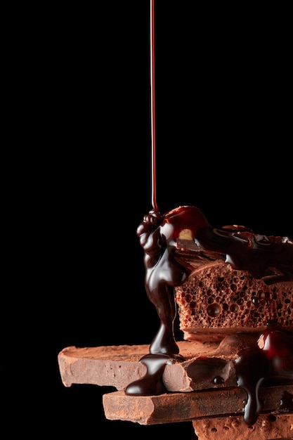 Фото Шоколадный сироп льется на кусочки темного шоколада, изолированные на черном