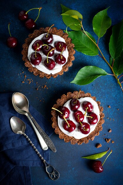 Chocolate tarts with cream and fresh berries of sweet cherry on a dark concrete table. Selective focus.Top view.