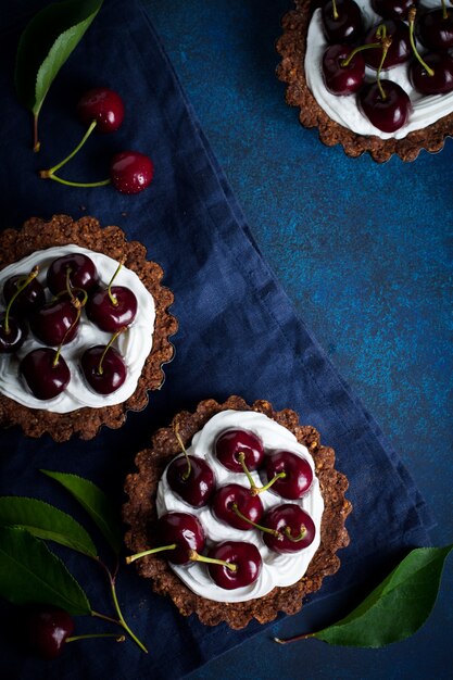 Chocolate tarts with cream and fresh berries of sweet cherry on a dark concrete table. Selective focus.Top view.