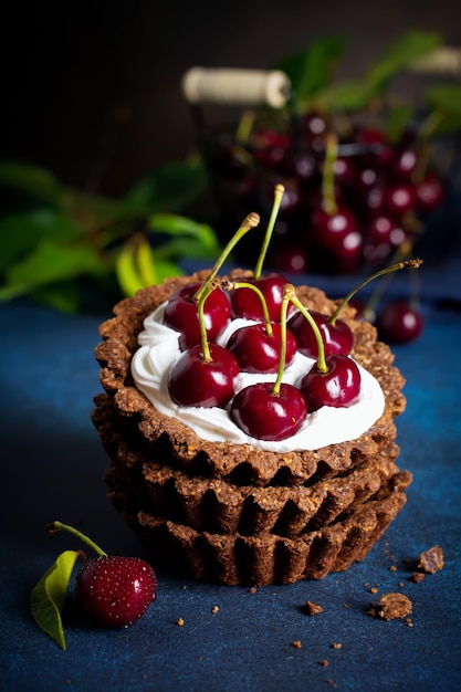 Chocolate tarts with cream and fresh berries of sweet cherry on a dark concrete table. Selective focus.