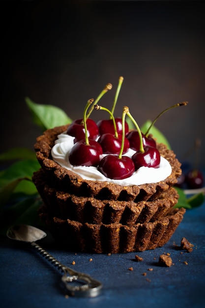 Chocolate tarts with cream and fresh berries of sweet cherry on a dark concrete table. Selective focus.