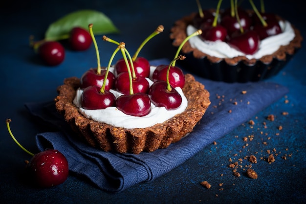 Chocolate tarts with cream and fresh berries of sweet cherry on a dark concrete table. Selective focus.