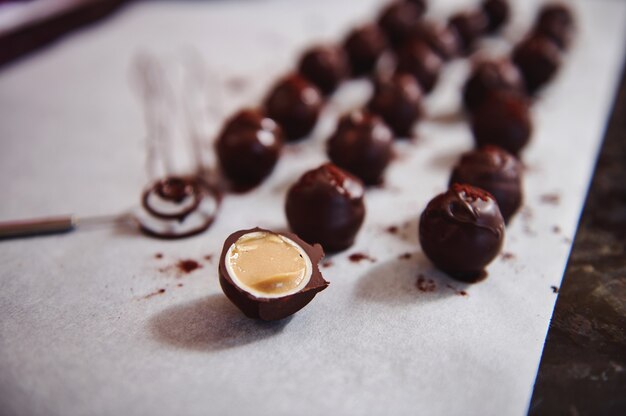 Chocolate truffles on parchment paper and accent in the foreground with chocolate candy cut in half and stuffed with salted caramel.