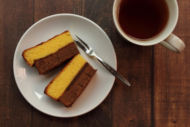 Chocolate and vanilla layered cake on white plate and a glass of tea