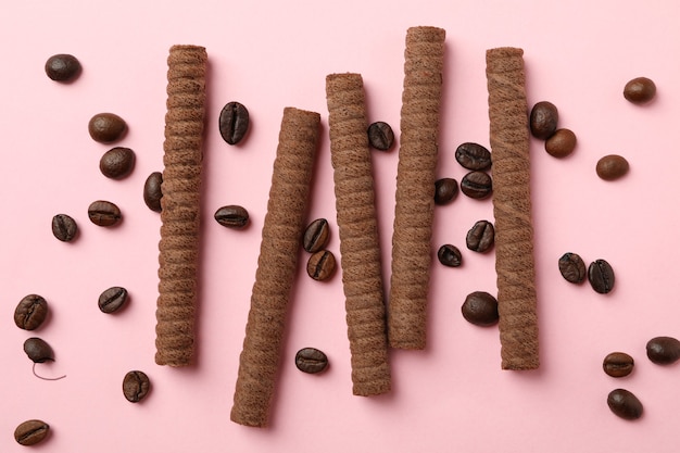 Rotoli di wafer al cioccolato e chicchi di caffè su sfondo rosa