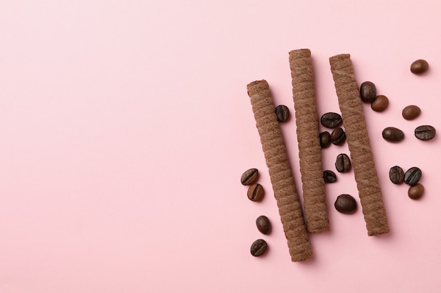 Chocolate wafer rolls and coffee beans on pink