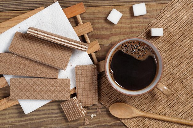 Chocolate waffles and cup of hot coffee on rustic wooden table, top view