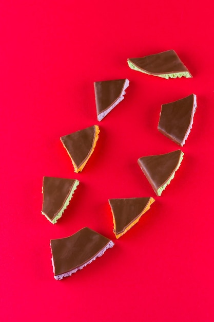 Фото Шоколад с фруктовой начинкой на красном фоне кусочки шоколада с чернилами, мятой и апельсином