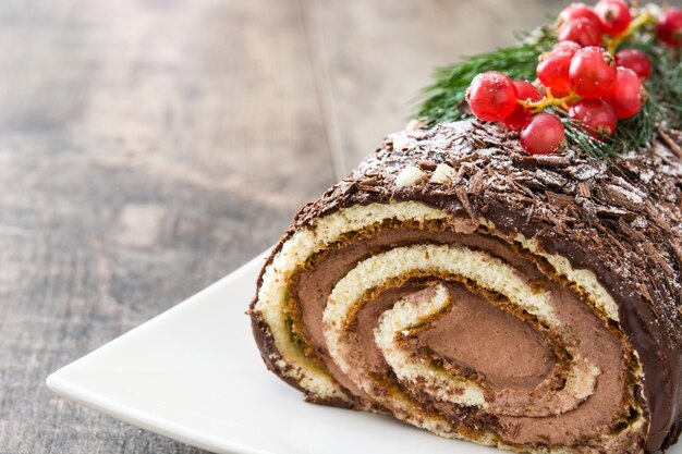 Photo chocolate yule log christmas cake with red currant on wooden  copyspace