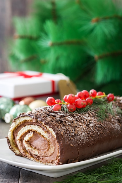 Foto torta di natale del ceppo del yule del cioccolato con il ribes su di legno.