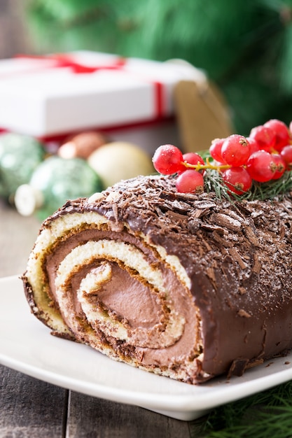 Chocolate yule log christmas cake with red currant on wooden .