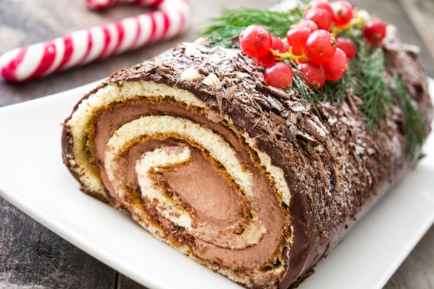 Foto torta di natale del ceppo del yule del cioccolato con il ribes su di legno.