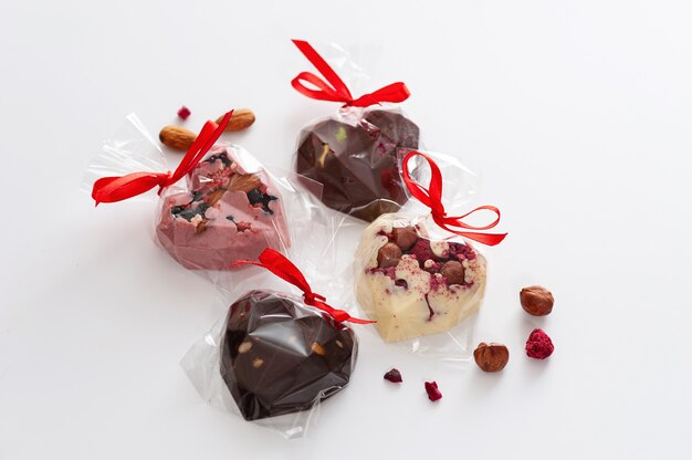 Chocolates mix, in the form of hearts with pink, milk and white chocolate with strawberries, blueberries and almonds, tied with a ribbon, handmade, top view, on a white background