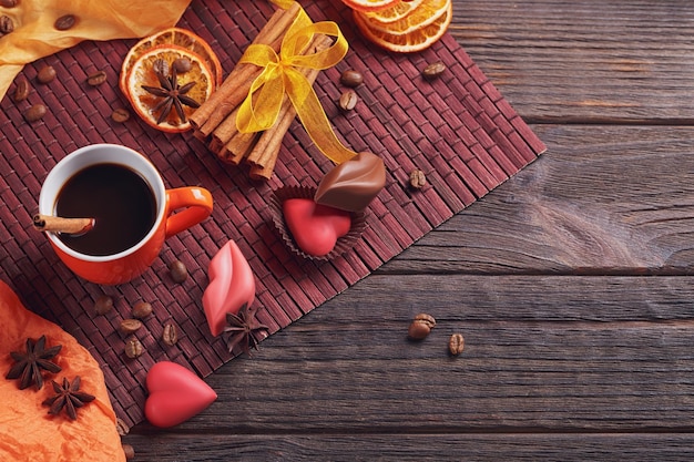 Chocolates in the shape of heart and lips orange cup of black coffee and spices on dark background