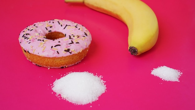 Ciambella scelta contro la banana: zucchero e calorie negli alimenti. iniziare a mangiare sano o cibo spazzatura. sfondo rosa