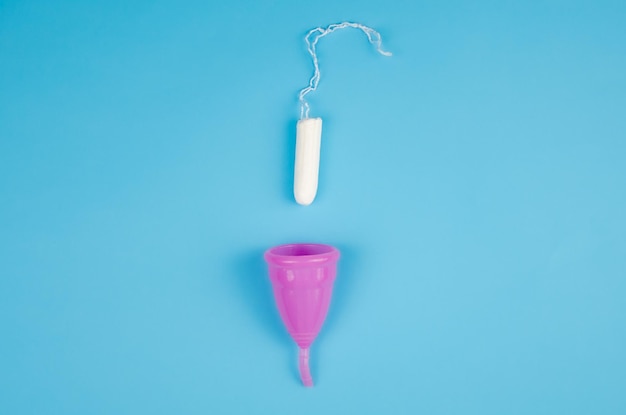 Фото На выбор: менструальная чаша или тампон. тампон женской гигиены и менструальная чаша на синем фоне. средства женской гигиены. выборочный фокус. гигиена и экология
