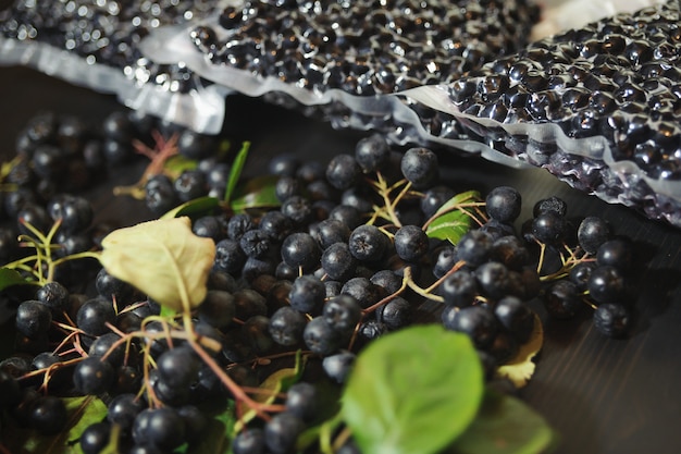 Foto le bacche di chokeberry (aronia melanocarpa) sono confezionate in sacchetti sottovuoto e bacche nere sul tavolo scuro.