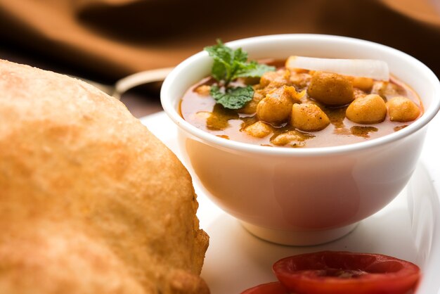 Chole Bhature or Chick pea curry and Fried  Puri served in terracotta crockery over white background. selective focus