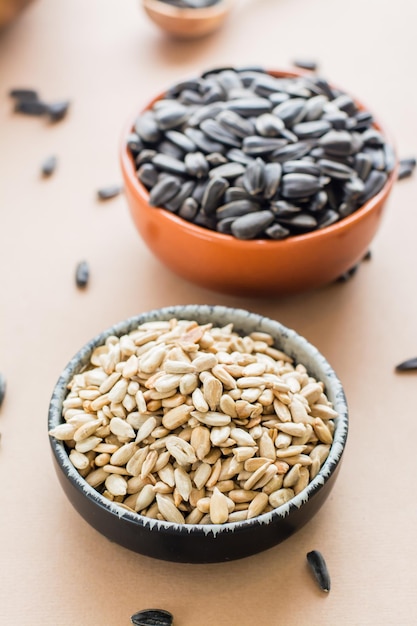 Choose between peeled and unpeeled sunflower seeds in bowls on the table. Natural source of vitamins and fat. Vertical view