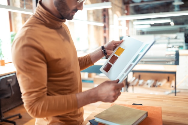 Choosing color. Close up of bearded writer wearing orange polo neck choosing color for the book cover