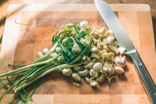 Chopped bunch of green garlic on wooden cutting board with knife