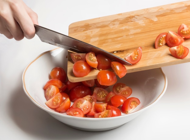 Chopped cherry tomatoes are transferred to a salad bowl.