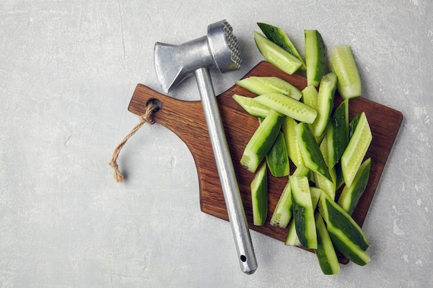 Chopped fresh cucumbers on a wooden cutting board with a kitchen chop with a hammer