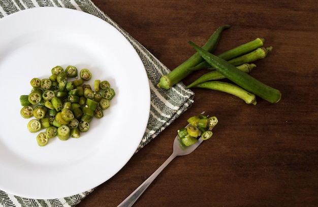 Chopped and fried okra inside a plate and on the fork next to raw okra