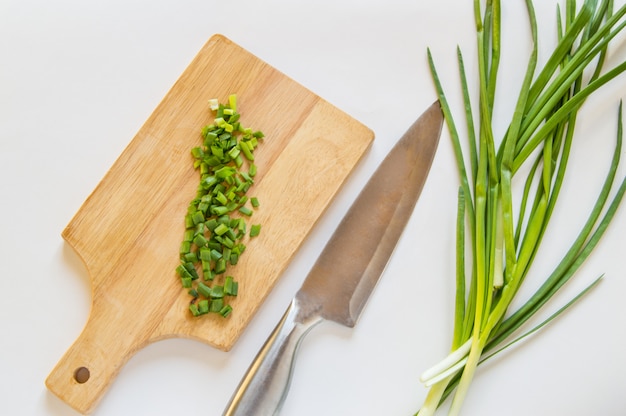 Cipolla verde tagliata sul bordo di legno, coltello su fondo isolato bianco