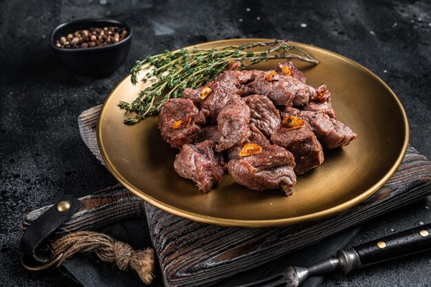 Chopped Grilled Diced Beef garlic steak on a plate with thyme Black background Top view