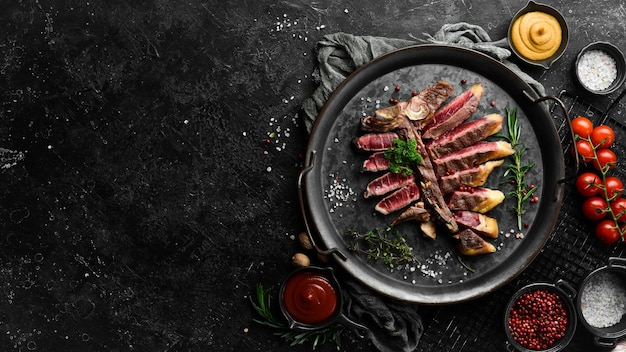 Chopped juicy porterhouse steak or T Bone Steak dry aged of beef Ready to Cook on wooden Board with herbs pepper and salt On a black stone background