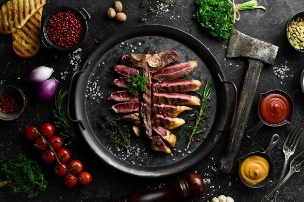 Chopped juicy porterhouse steak or T Bone Steak dry aged of beef Ready to Cook on wooden Board with herbs pepper and salt On a black stone background