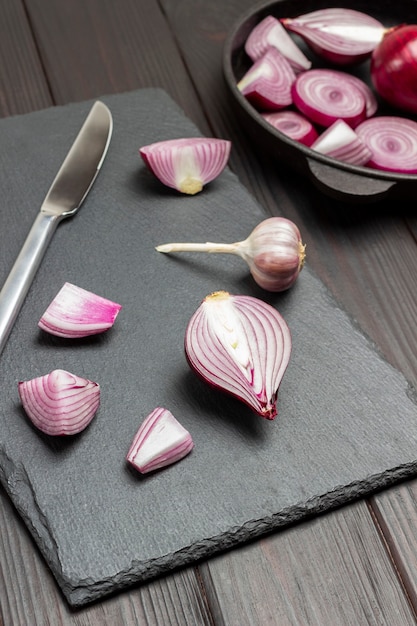 Chopped onion and knife on cutting board. Sliced purple onions in bowl. Dark wooden background. Top view