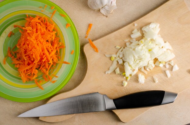 Photo chopped onion on a wooden cutting board and grated carrot on the plate and knife