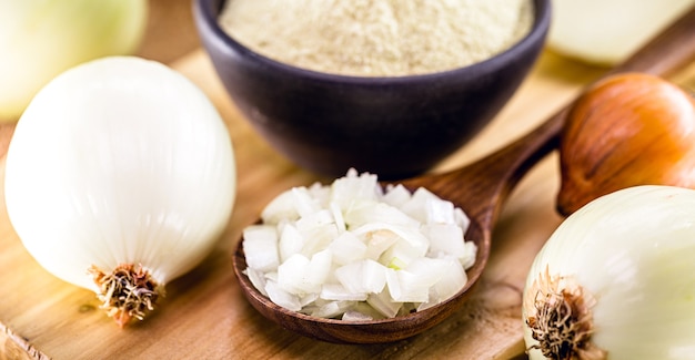 Chopped onion in wooden spoon with powdered onion pot in the background