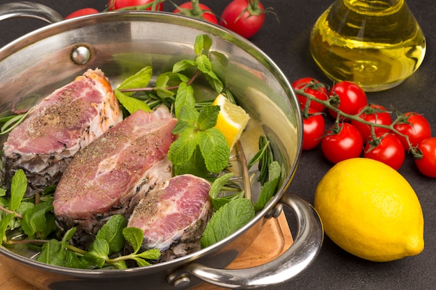 Chopped river fish with mint and rosemary in pan. Tomatoes, lemon and glass bottle with oil