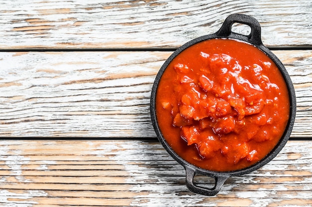 Chopped tinned red tomatoes in a pan. White background. Top view. Copy space.