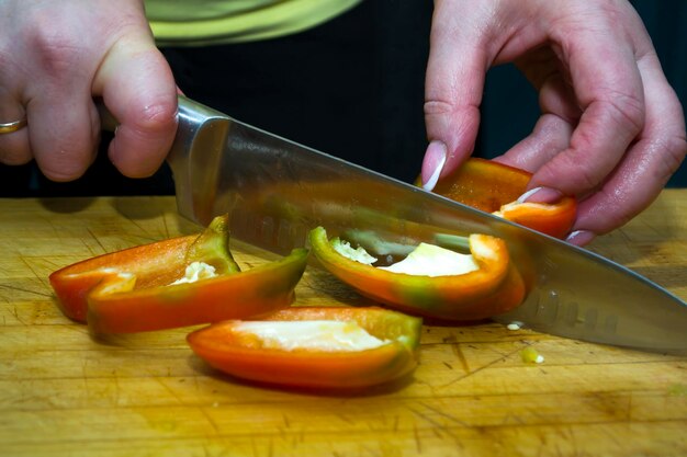 Photo chopped yellow red and green peppers and a kitchen knife on a wooden board isolated on white